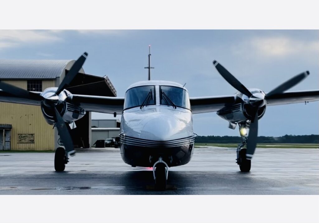 Sleek Twin-Engine Aircraft On The Tarmac With A Muted Yellow Hangar In The Background.