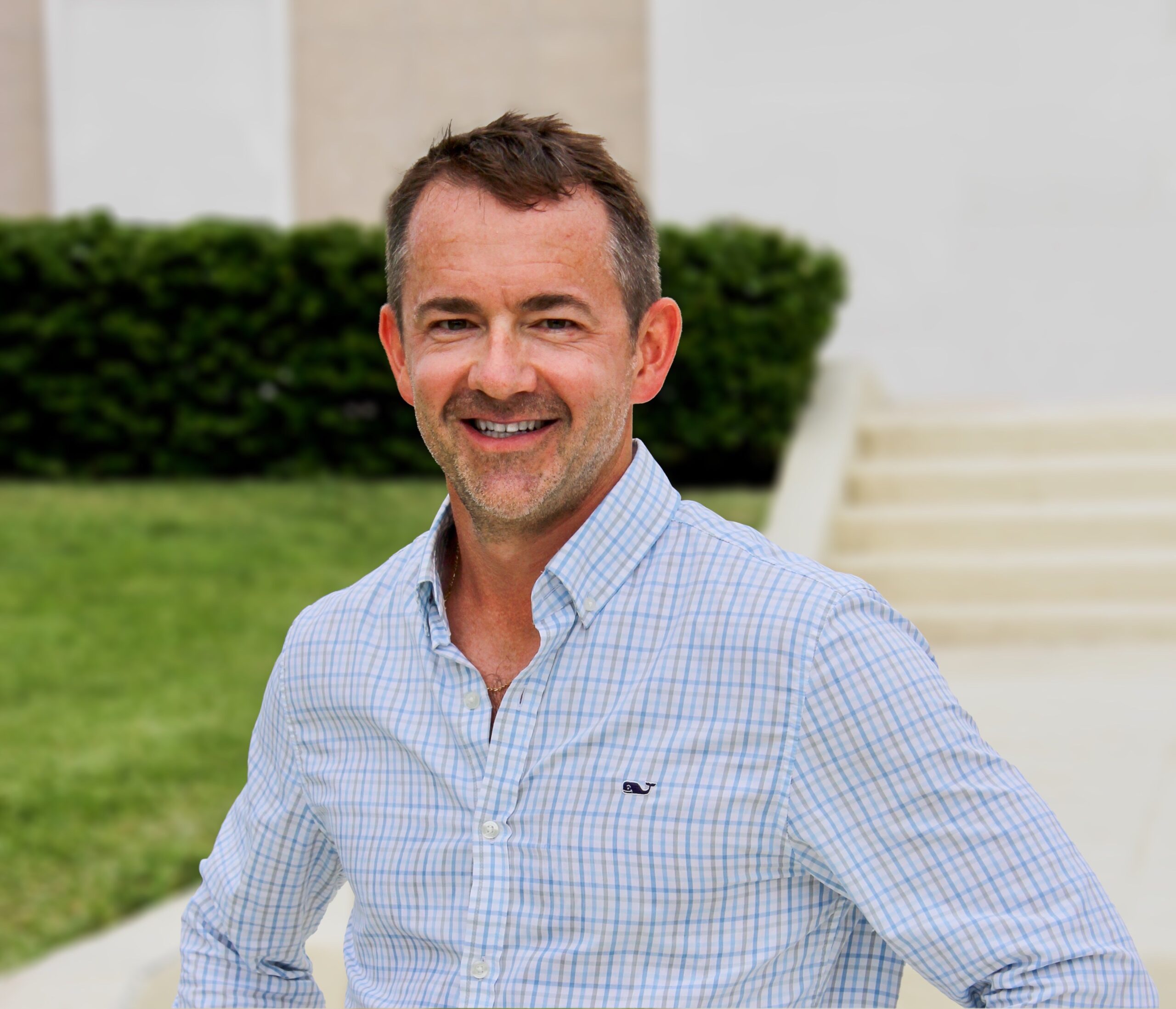 Smiling Man In A Light Blue Shirt, Outdoors, Exuding Friendliness And Professionalism.