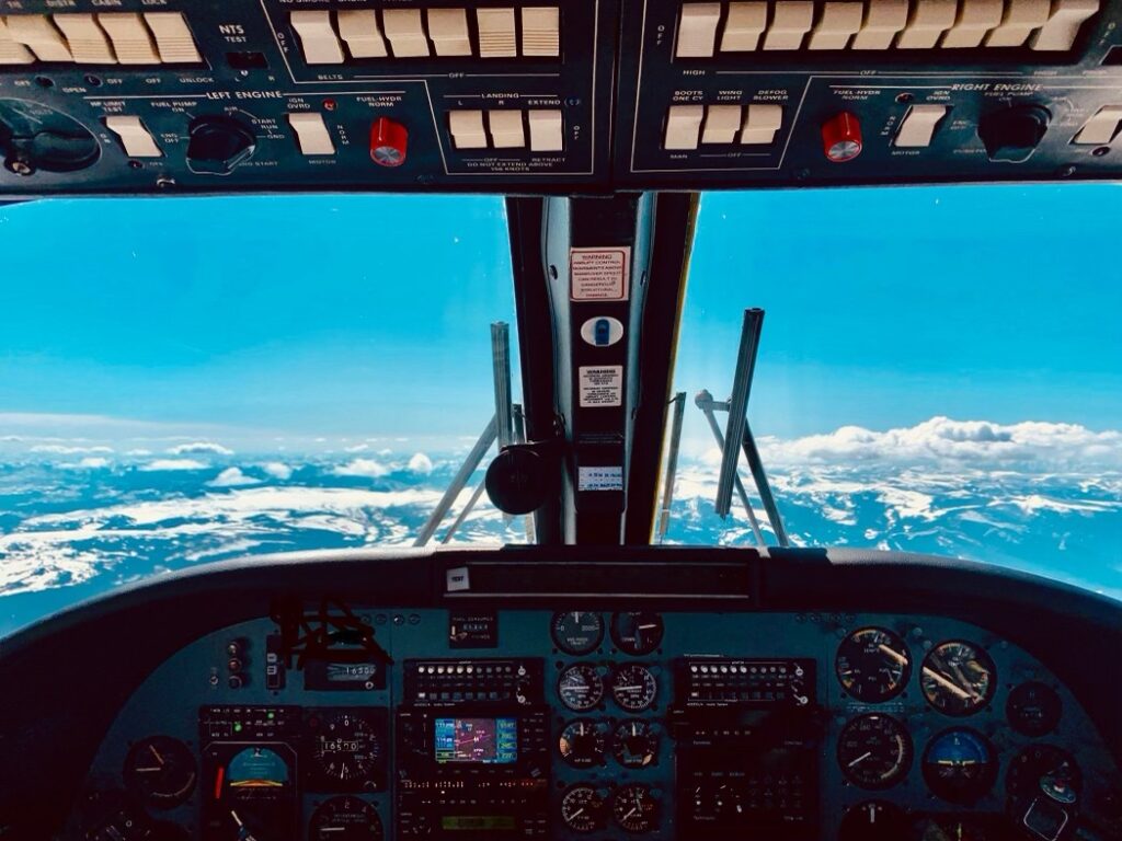 Stunning Cockpit View Of Snow-Capped Mountains Beneath A Vibrant Blue Sky With Fluffy Clouds.